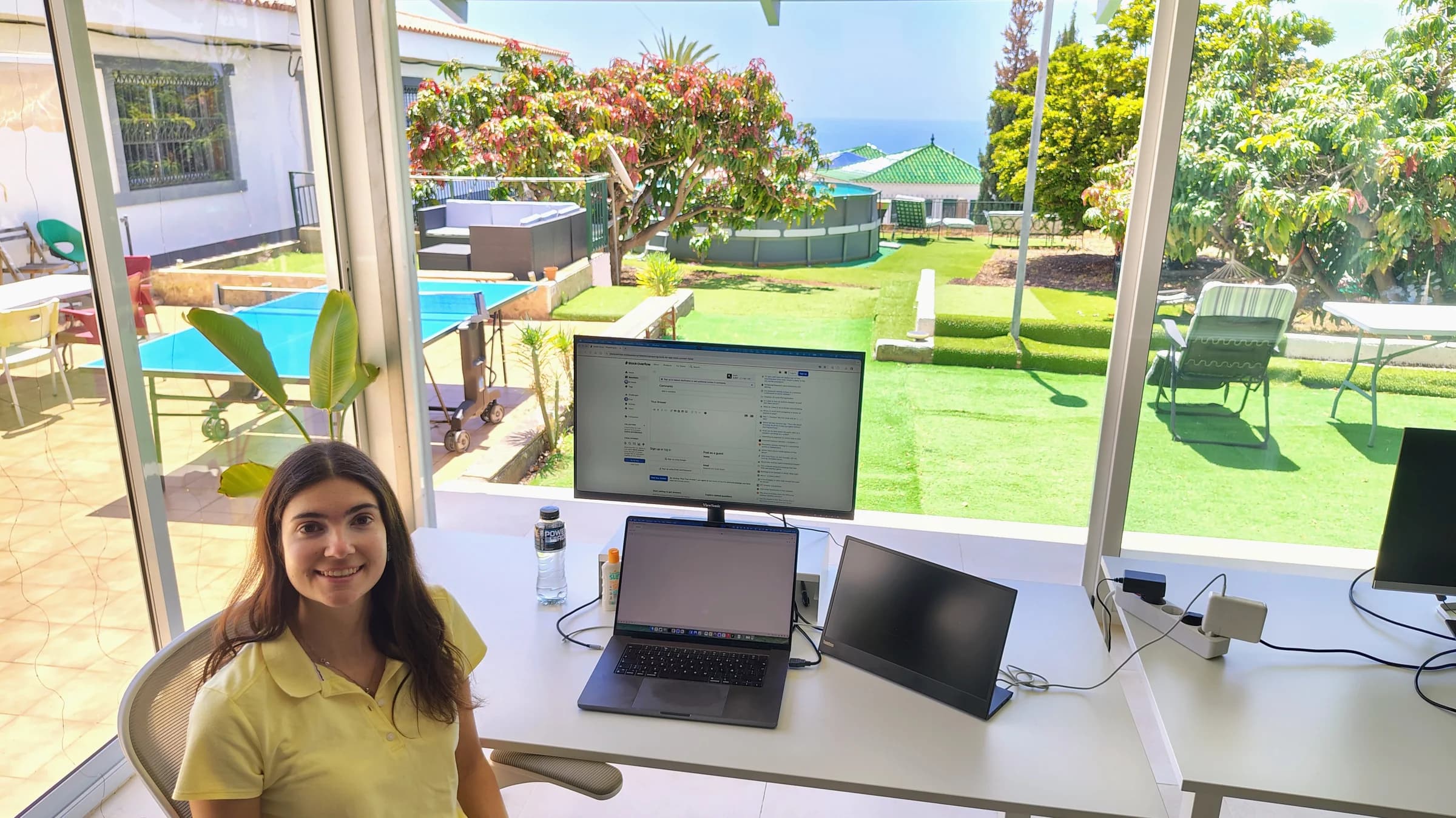 Selene at a desk with a laptop and monitors, overlooking Blue Paradise’s garden, pool and the Atlantic