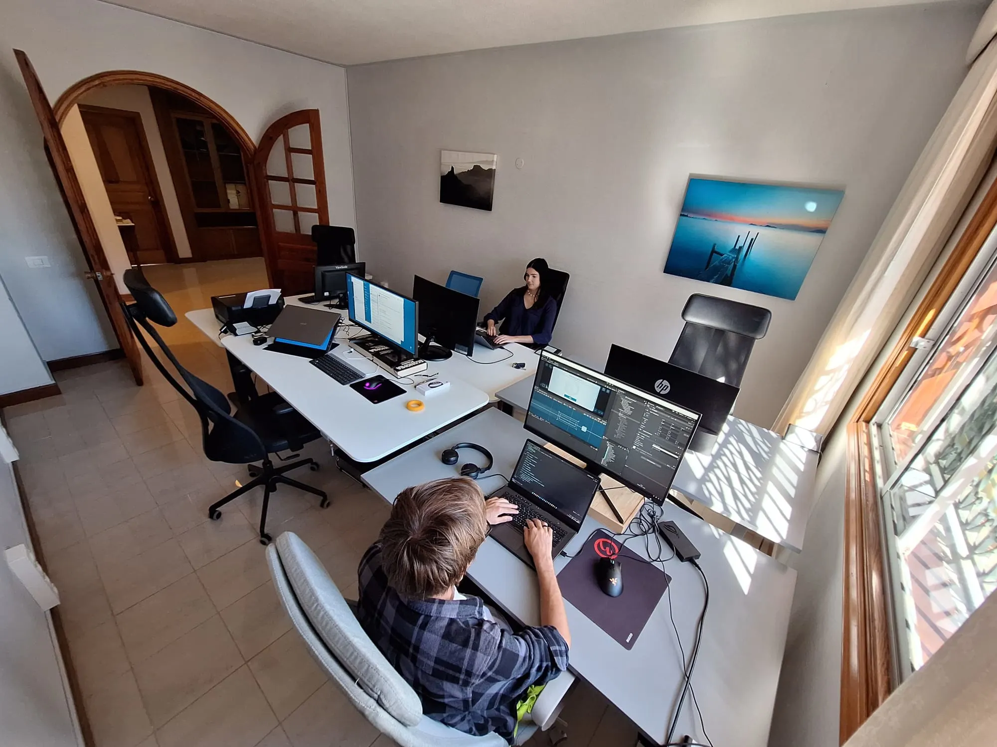 Espace de coworking intérieur avec bureaux, écrans et vue sur le jardin.